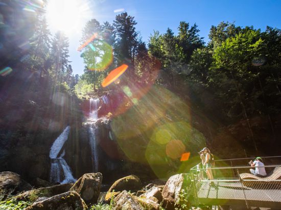 Touristen stehen auf einer Aussichtsplattform und blicken auf eine Stufe der Triberger Wasserfälle.