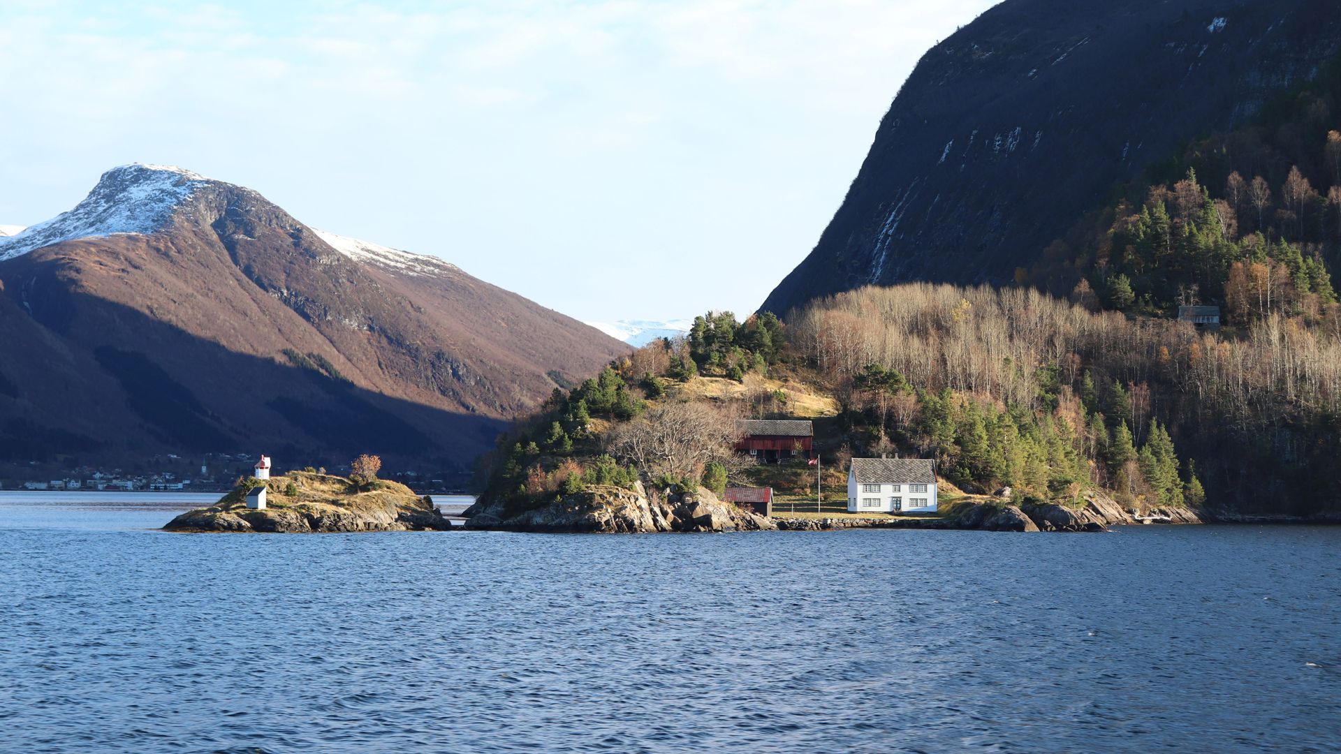 Kleiner Leuchtturm und weißes Haus am Rande des Fjords.