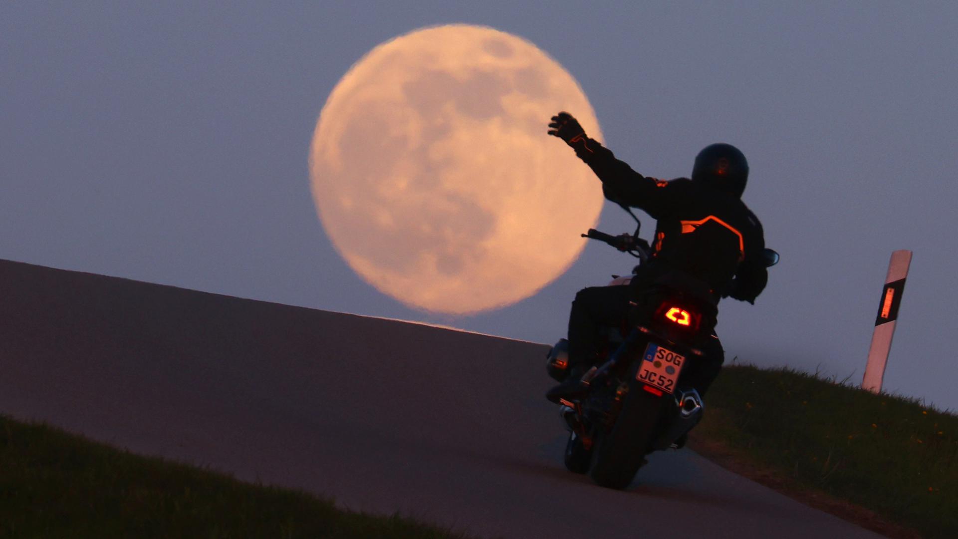 Ein Motorradfahrer fährt vor dem aufgehenden Vollmond über eine Hügelkuppe. Am 27. April 2021 kommt es zu einem sogenannten "Supermond". Dann ist die Entfernung zwischen Mond und Erde geringer als sonst. +++ dpa-Bildfunk +++