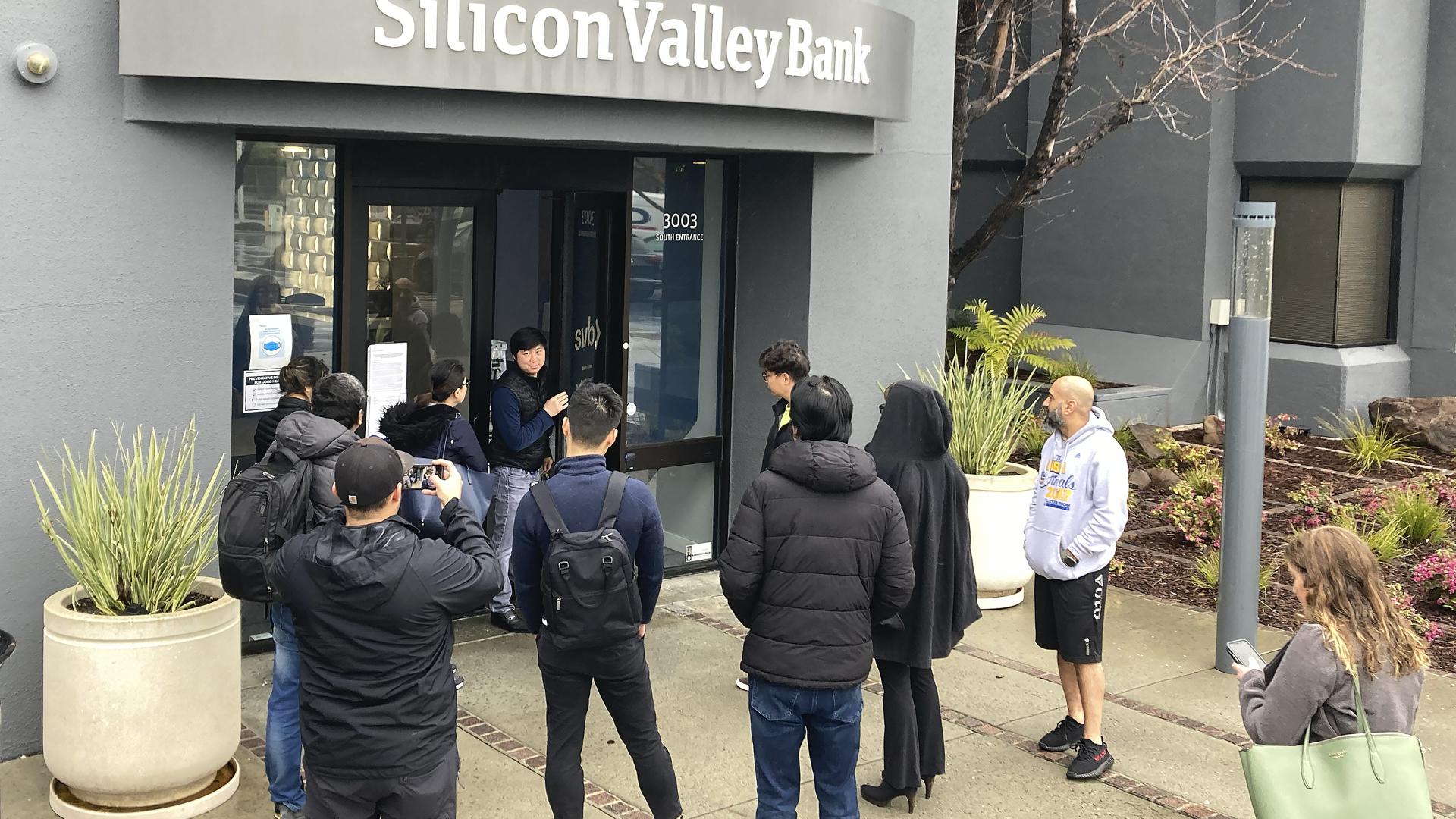 Eine Person, die aus dem Inneren der Silicon Valley Bank (M) kommt, spricht mit Menschen, die vor dem Eingang der Silicon Valley Bank (SVB) warten. Das auf Start-up-Finanzierung spezialisierte US-Geldhaus Silicon Valley Bank (SVB) ist nach einer gescheiterten Notkapitalerhöhung vorübergehend geschlossen und unter staatliche Kontrolle gestellt worden. +++ dpa-Bildfunk +++