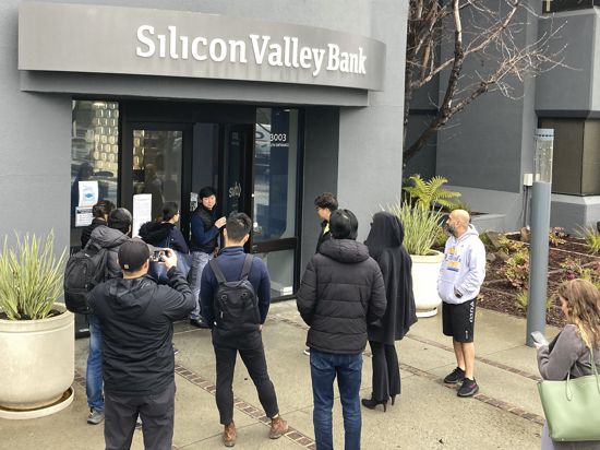 Eine Person, die aus dem Inneren der Silicon Valley Bank (M) kommt, spricht mit Menschen, die vor dem Eingang der Silicon Valley Bank (SVB) warten. Das auf Start-up-Finanzierung spezialisierte US-Geldhaus Silicon Valley Bank (SVB) ist nach einer gescheiterten Notkapitalerhöhung vorübergehend geschlossen und unter staatliche Kontrolle gestellt worden. +++ dpa-Bildfunk +++