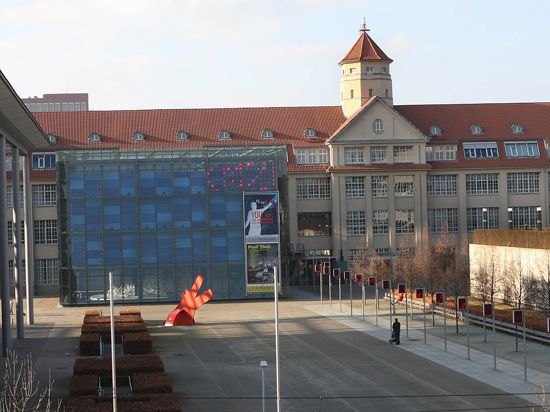 Außenansicht des Zentrums für Kunst und Medien (ZKM) in Karlsruhe mit seinem blauen Glaswürfel-Anbau und der roten Kunstskulptur auf dem Vorplatz. 