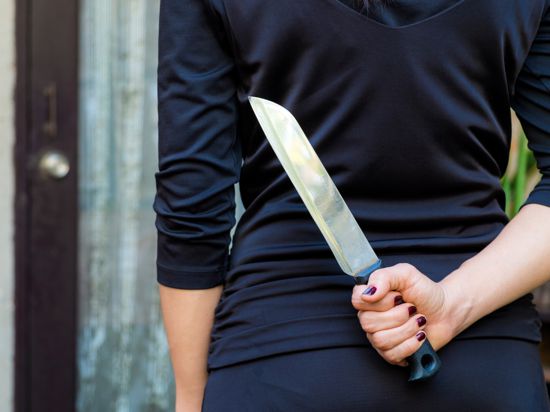 Woman in black holding a knife hidden behind