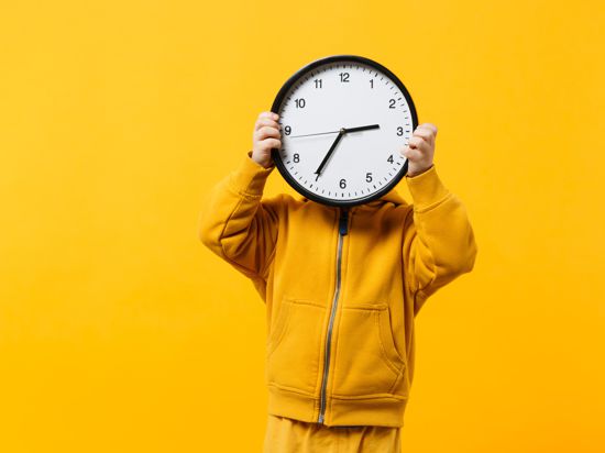 Little kid boy 3-4 years old wearing yellow clothes hold clock isolated on orange wall background, children studio portrait. People sincere emotions, childhood lifestyle concept. Mock up copy space