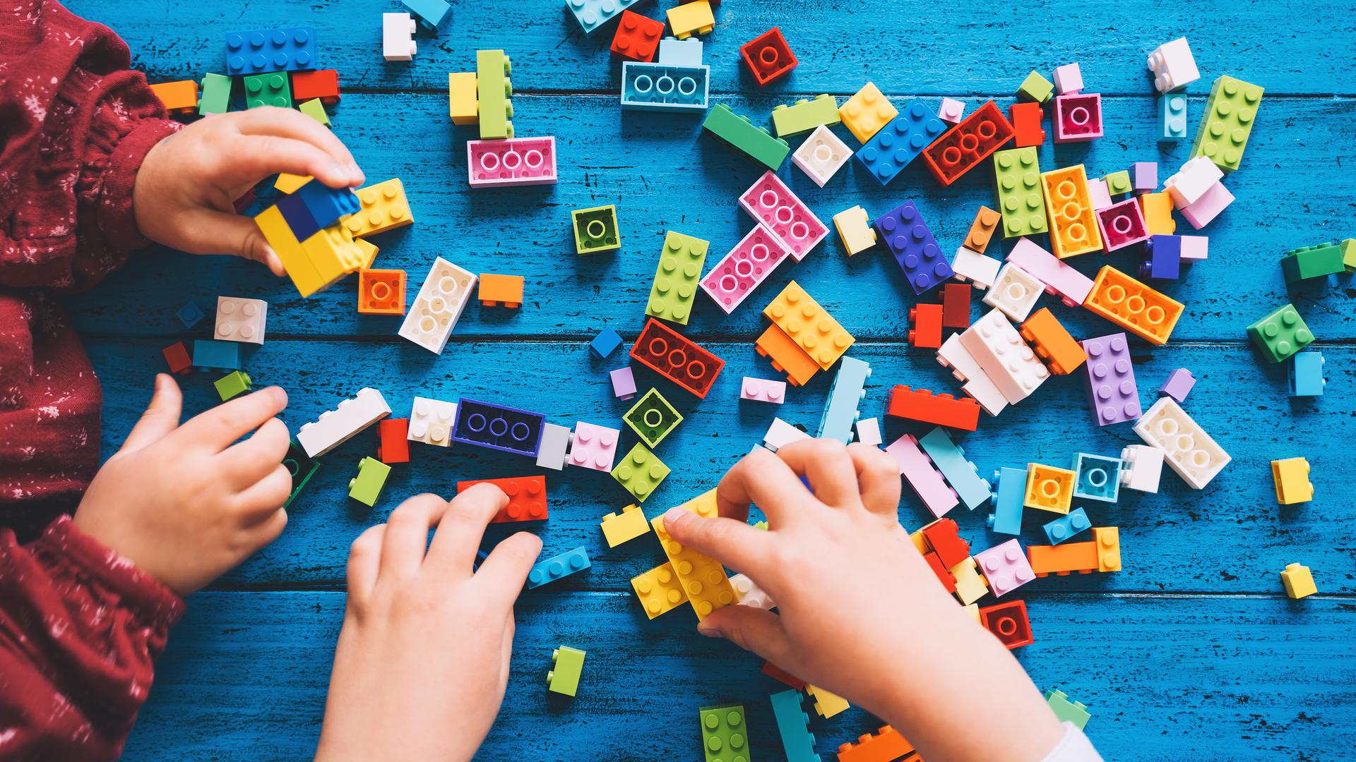 Children play and build with colorful toy bricks or plastic blocks on table. School or preschool background. Concept of kids leisure and education at home or class, early learning and development.