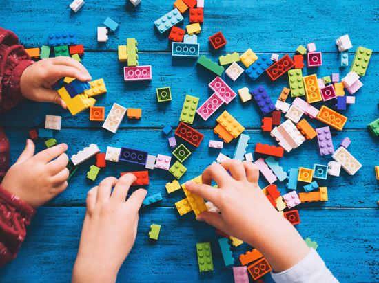 Children play and build with colorful toy bricks or plastic blocks on table. School or preschool background. Concept of kids leisure and education at home or class, early learning and development.