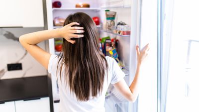 Frau steht fragend vor Kühlschrank