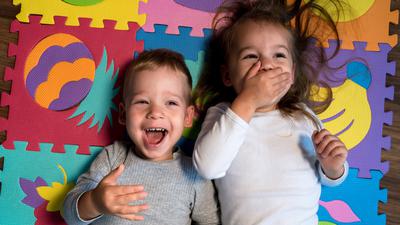childhood, family friendship, games - close up portrait Two funny joy happy smiling little toddler peschool kids siblings twins brother with sister have fun lie laughing on puzzles mat at home indoors.