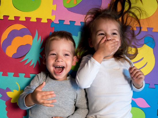 childhood, family friendship, games - close up portrait Two funny joy happy smiling little toddler peschool kids siblings twins brother with sister have fun lie laughing on puzzles mat at home indoors.