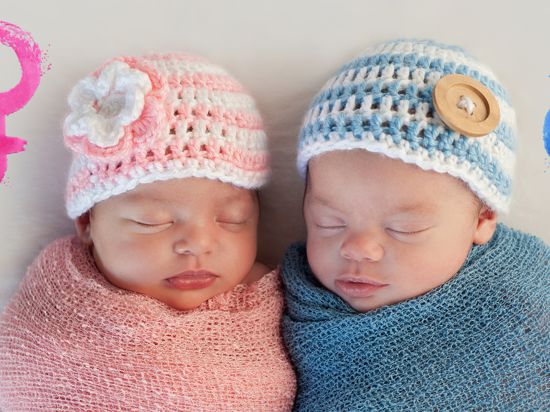 Zwei Babys liegen nebeneinander, das linke trägt rosa Kleidung, das rechte blaue.