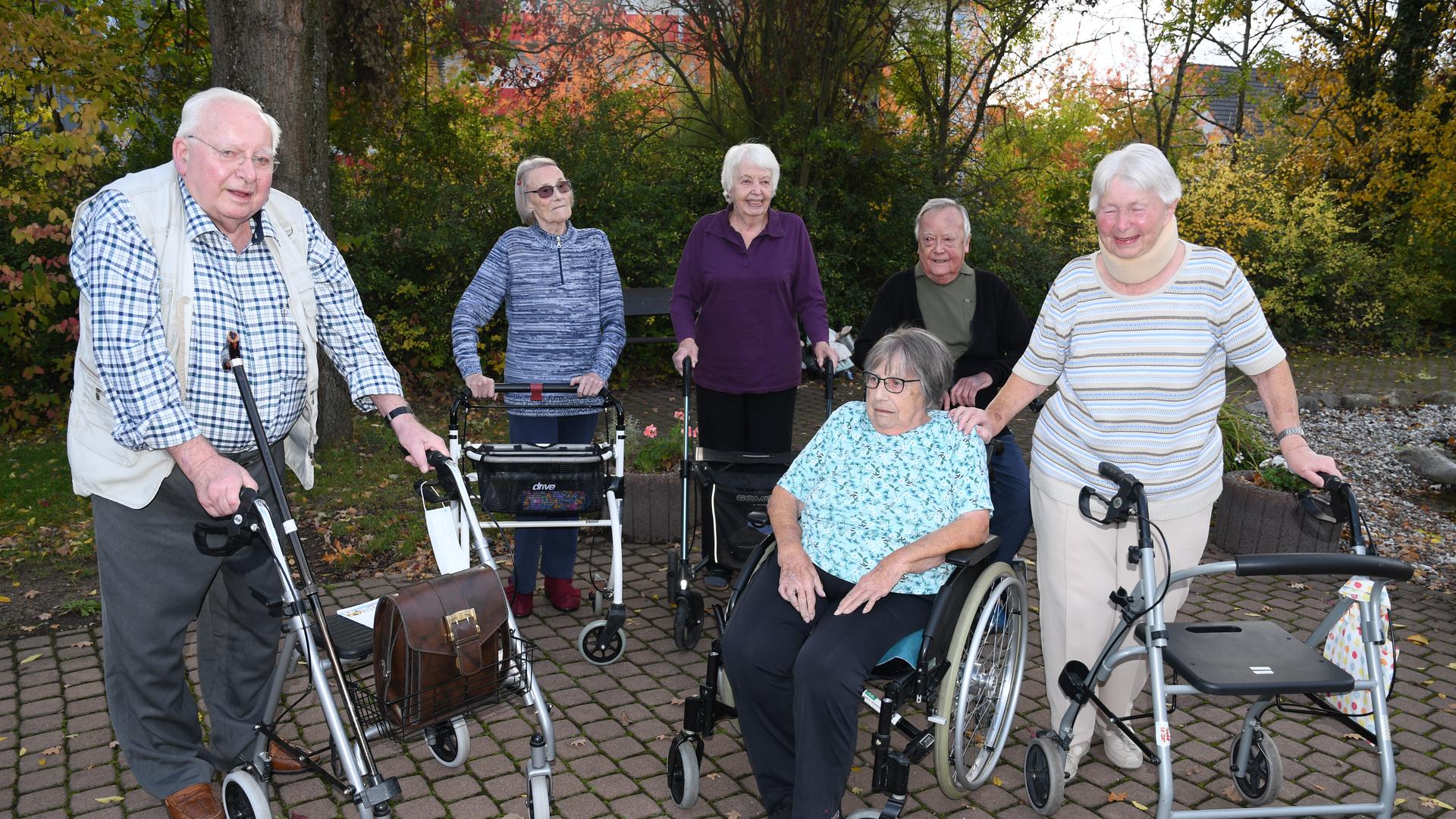Sechs Heimbewohner sind miteinander im Garten. Fünf stützen sich auf Rollatoren, eine Dame sitzt im Rollstuhl.
