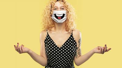 Happy laugh. Portrait of young caucasian woman with emotion on her protective face mask isolated on studio background. Beautiful female model. Human emotions, facial expression, sales, ad concept.
