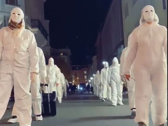 Weiß gekleidete Personen mit weißen Gesichtsmasken laufen in zwei Reihen hintereinander die Bürgerstraße in Karlsruhe entlang.