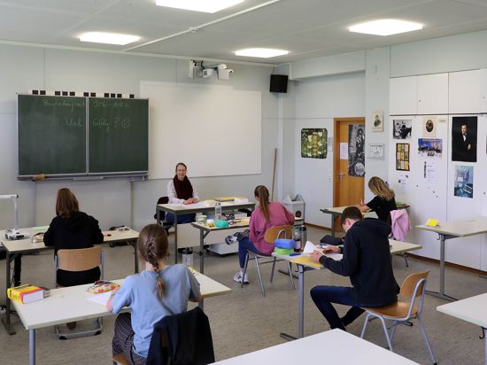 Schüler sitzen mit Abstand in einer Klasse, vorne sitzt die Lehrerin am Tisch.