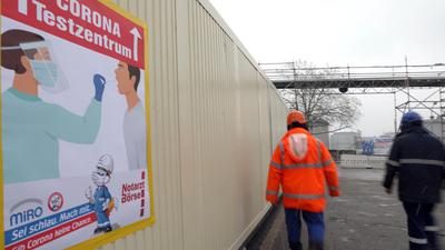 Arbeiter laufen bei der Raffinerie Miro in Karlsruhe an einem Schild vorbei, das auf ein Corona-Testzentrum hinweist.