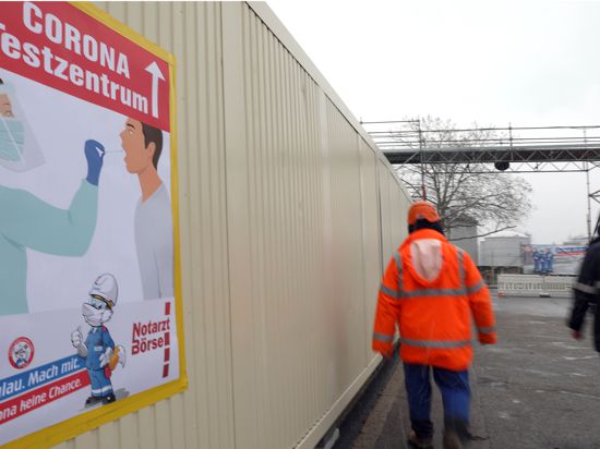 Arbeiter laufen bei der Raffinerie Miro in Karlsruhe an einem Schild vorbei, das auf ein Corona-Testzentrum hinweist.