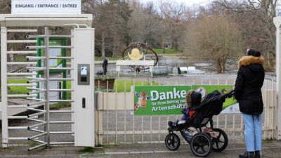 Frau steht mit Kinderwaren vor dem geschlossenen Haupteingang des Karlsruher Zoos.