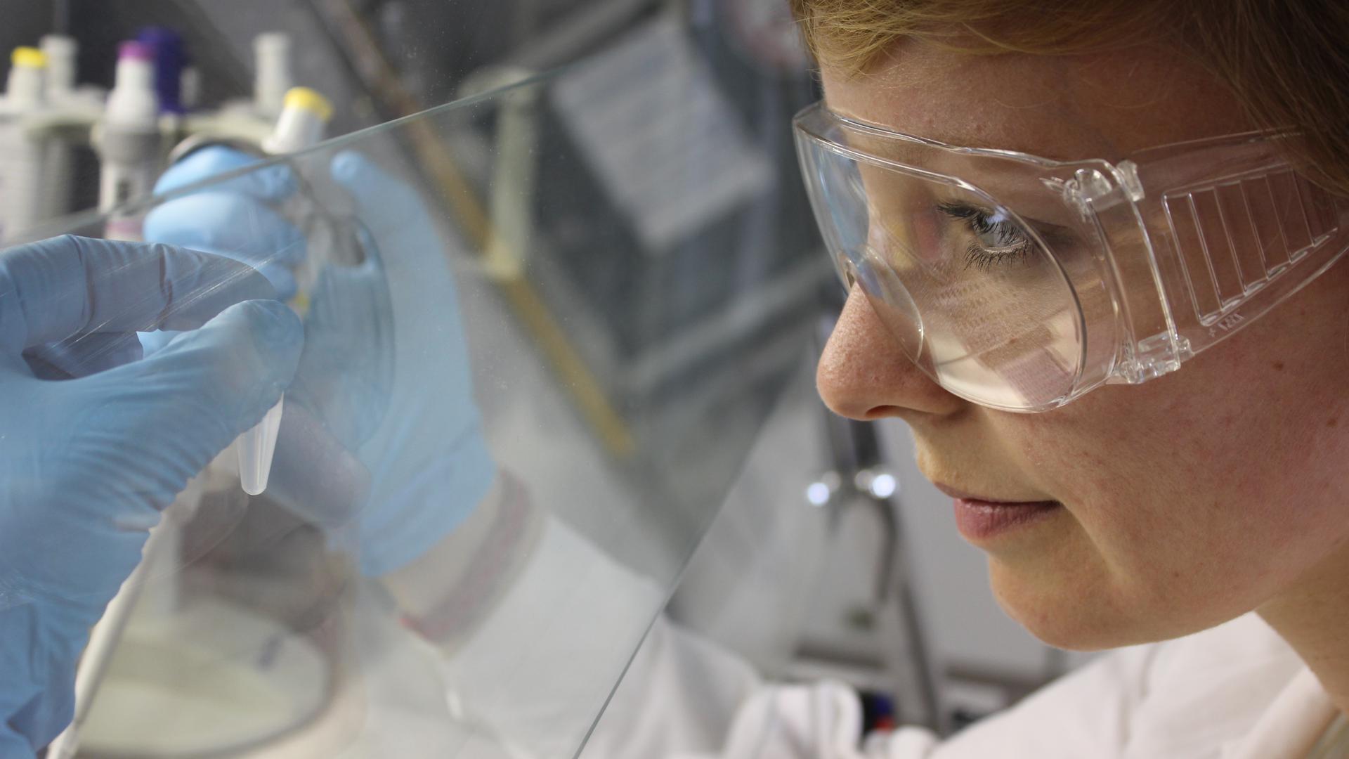 Frau in weißem Kittel, Schutzbrille und Handschuhen bei Laborarbeit