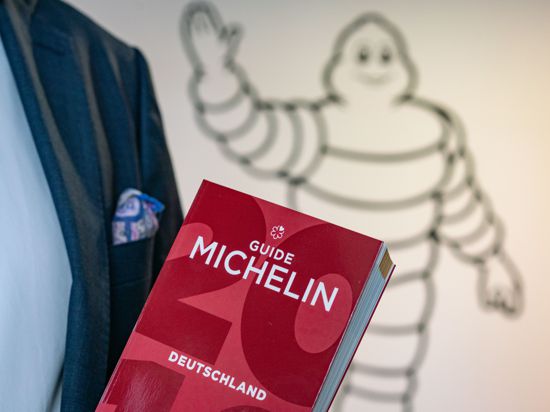Ein Mann hält einen roten „Guide Michelin“ in der Hand.
