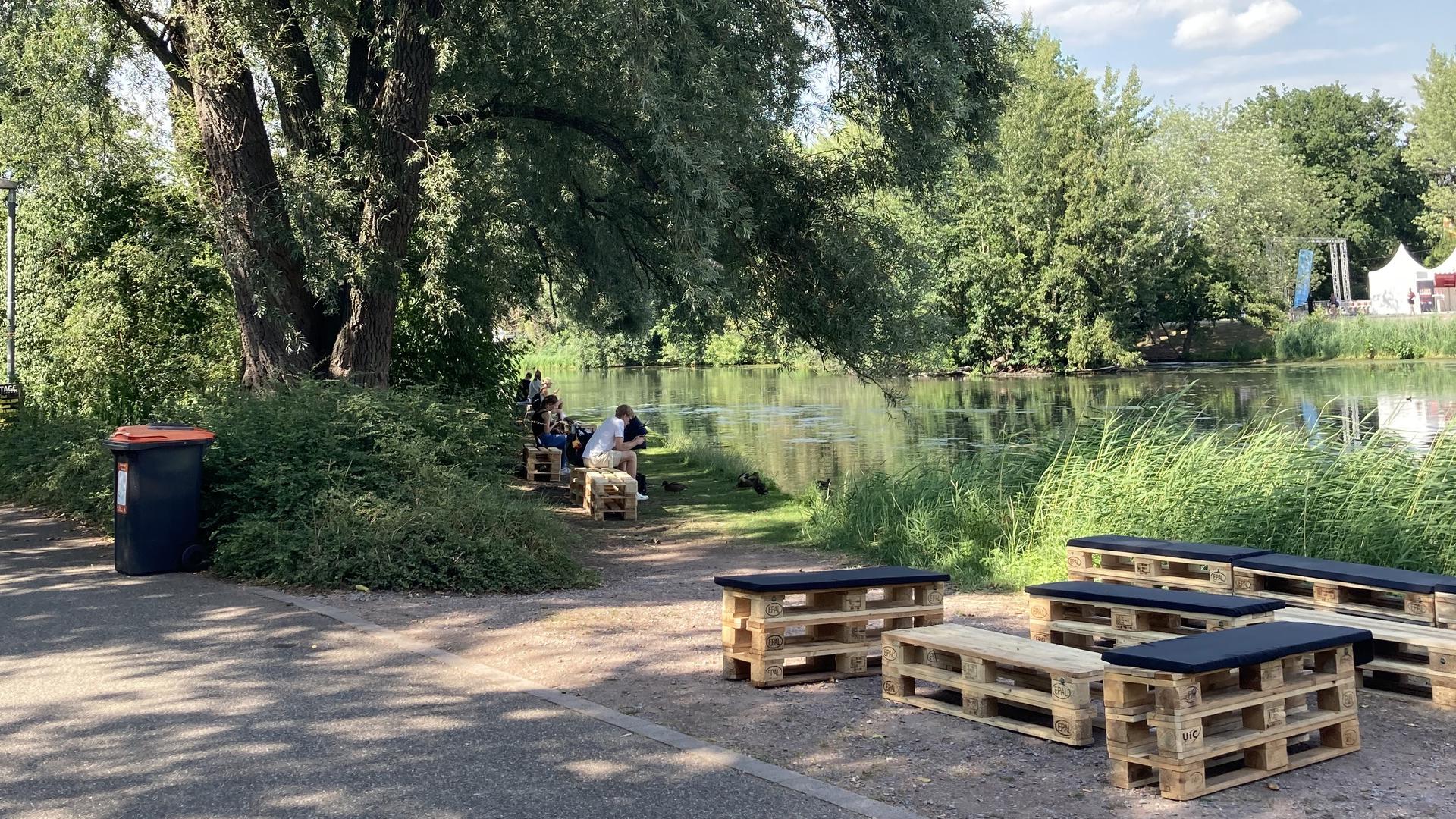 Menschen sitzen auf Holzbänken an einem See