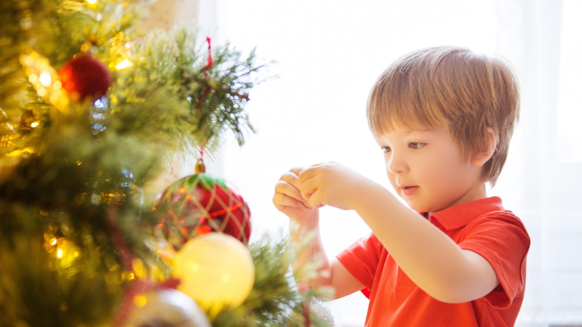 Kleiner Junge schmückt Weihnachtsbaum.