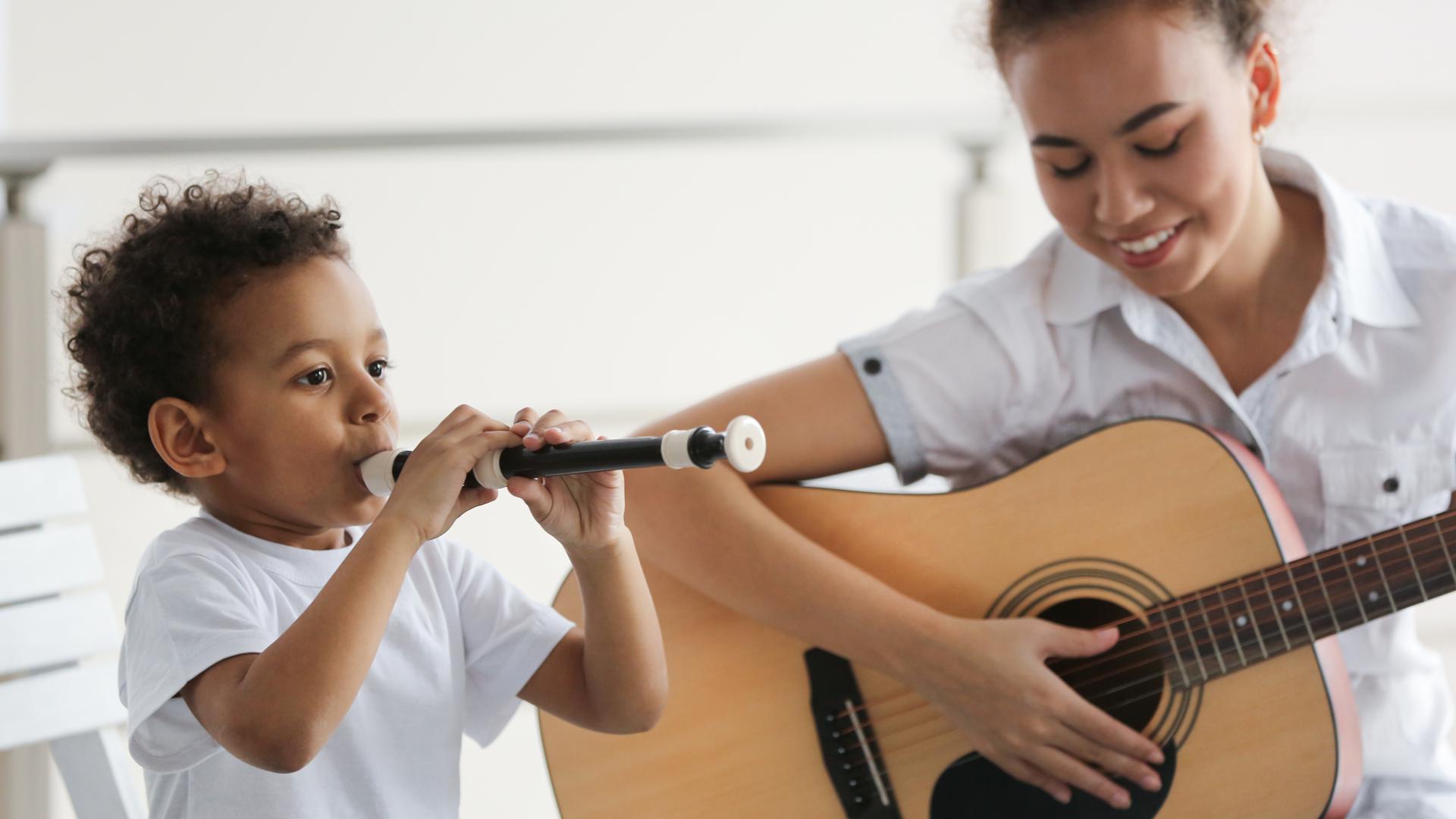 Junge an der Blockflöte und junges Mädchen mit Gitarre spielen zusammen