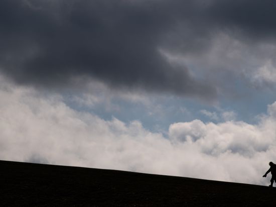 Zwei Kinder laufen auf einen Hügel am Kronsberg, während bei stürmischen Wetter dunkle Wolken am Horizont vorüberziehen. 