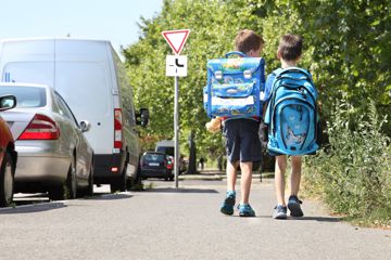 Zwei Kinder mit Schulranzen gehen die Straße entlang.