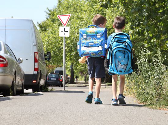 Zwei Kinder mit Schulranzen gehen die Straße entlang.