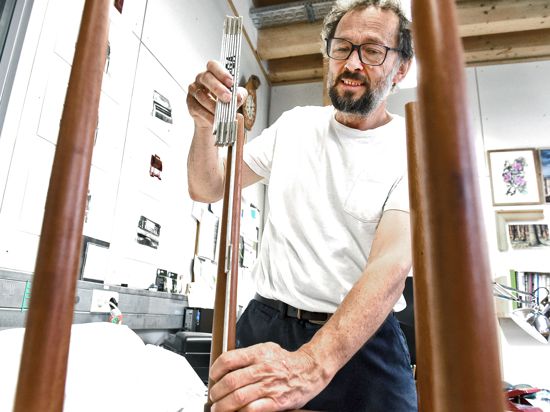 Ein Mann zeigt an einem Meterstab die Länge eines hölzernen Möbelbeins.