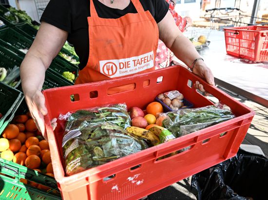  Eine Mitarbeiterin des Tafel-Ladens trägt eine Kiste voll mit Obst und Gemüse. 