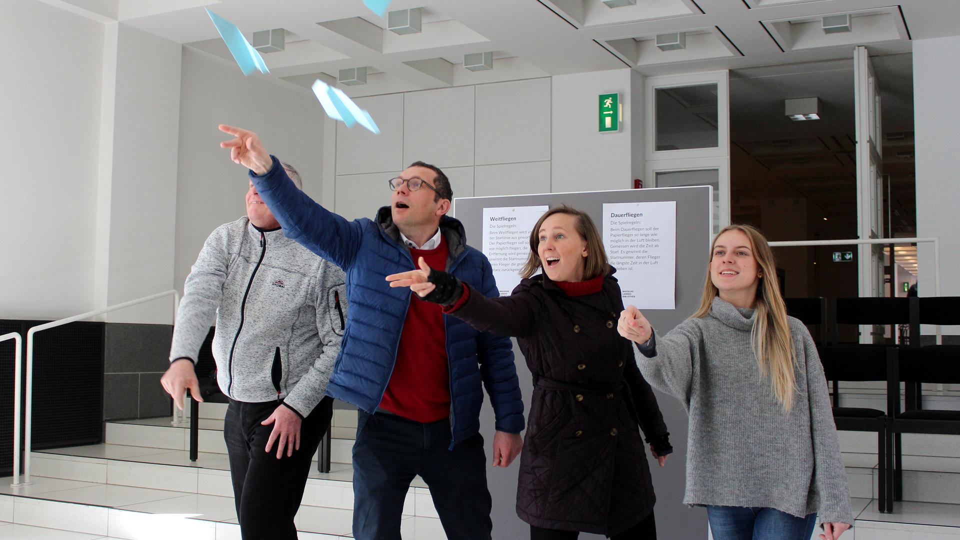 Vier Personen entlassen in der Badischen Landesbibliothek Karlsruhe ihre selbst gebastelten Papierflieger in die Luft.