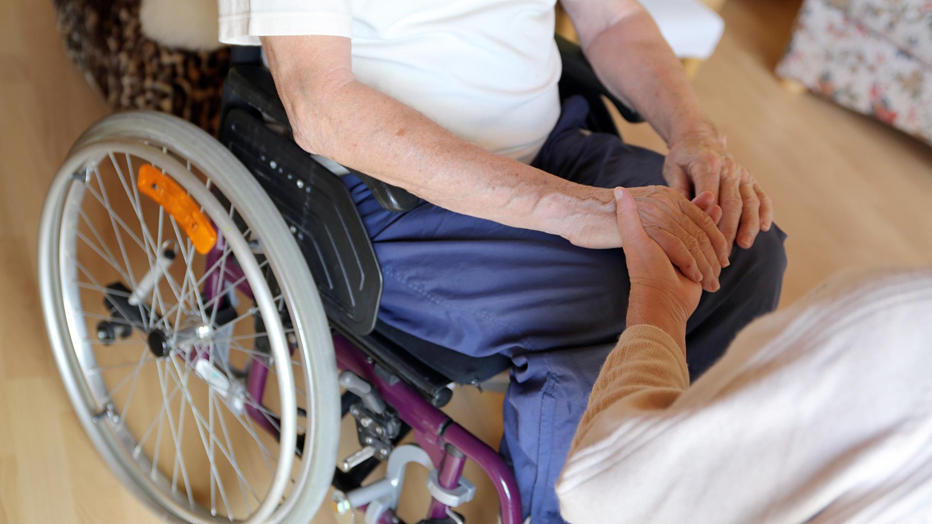 Mann im Rollstuhl hält die Hand einer Pflegerin.