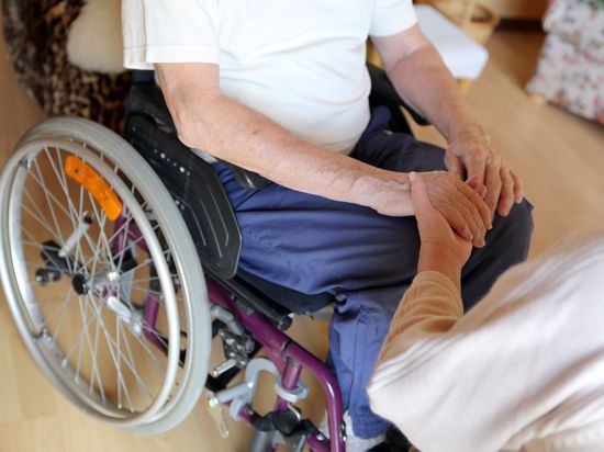 Mann im Rollstuhl hält die Hand einer Pflegerin.