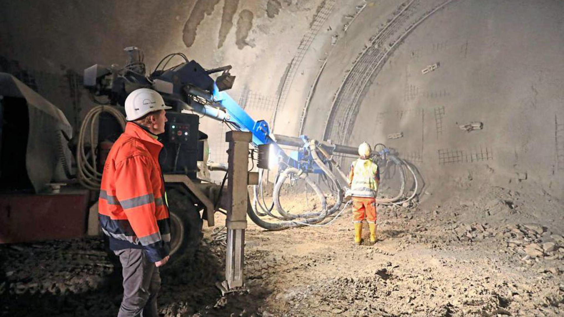 Mit Spritzbeton und Ankern wird die Ortsbrust stabilisiert, die Wand im vorderen Bereich des Tunnels. Ein Arbeiter (rechts) bedient die Spritzbetonmaschine.