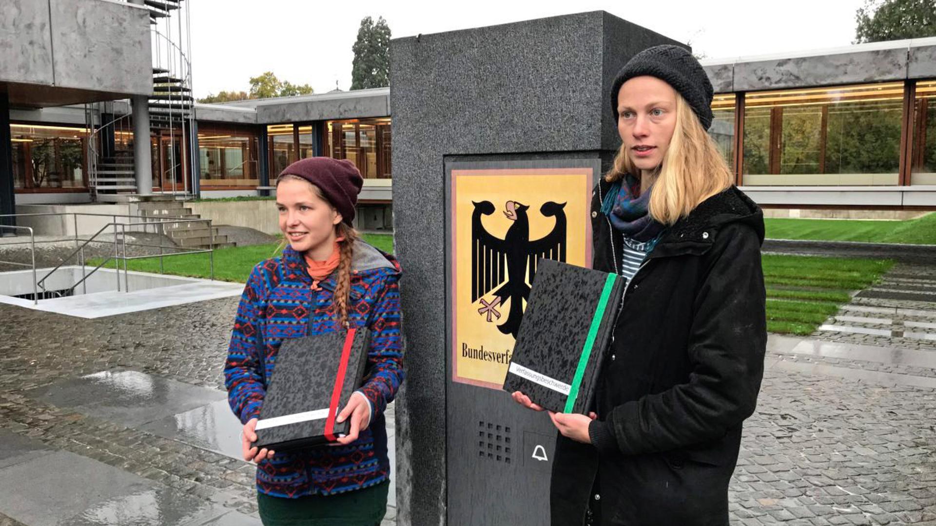 Franziska S. und Caroline K. werfen ihre Verfassungsbeschwerde in Form von zwei dicken Stapeln Papier am Karlsruher Bundesverfassungsgericht ein.