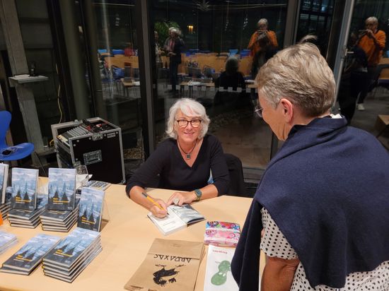 Frau signiert an einem Tisch mit Büchern ein Buch
