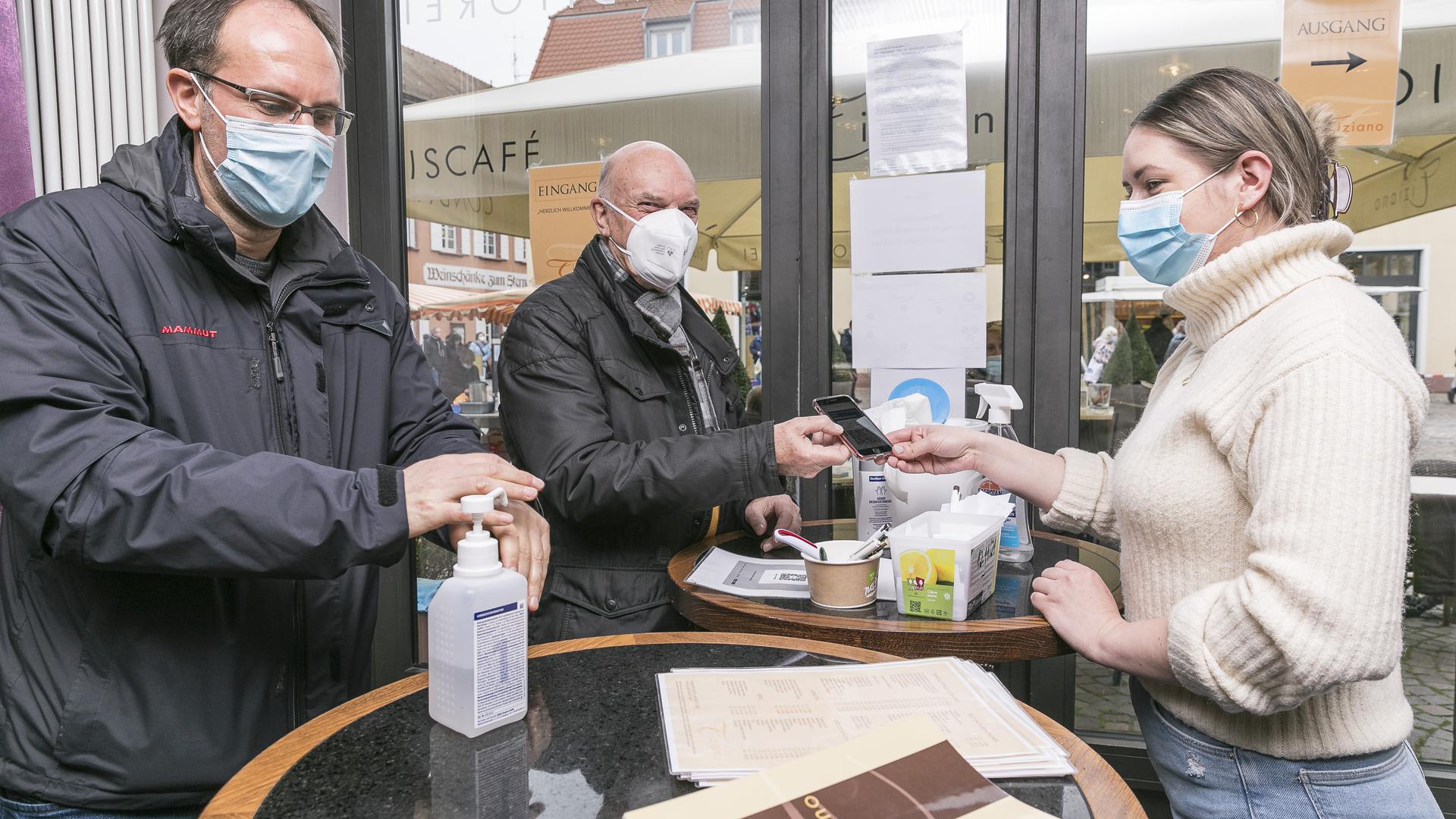 Impfausweis und Händedesinfektion: Michael und Willi Rutschmann (von links) werden am Eingang des Eiscafé Tiziano von Filialleiterin Karina Kandora kontrolliert.