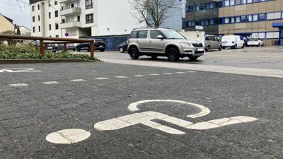 Im Vordergurnd ein Parkplatz für Schwerbehinderte, auf der Straße fährt ein Auto vorbei.