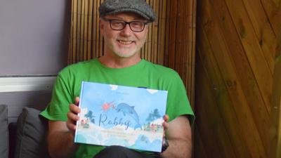 Michael Wollhöwer zeigt sein Buch „Robby aus Ettlingen und die Abenteuer des kleinen Delfins auf der Reise zum Glück“