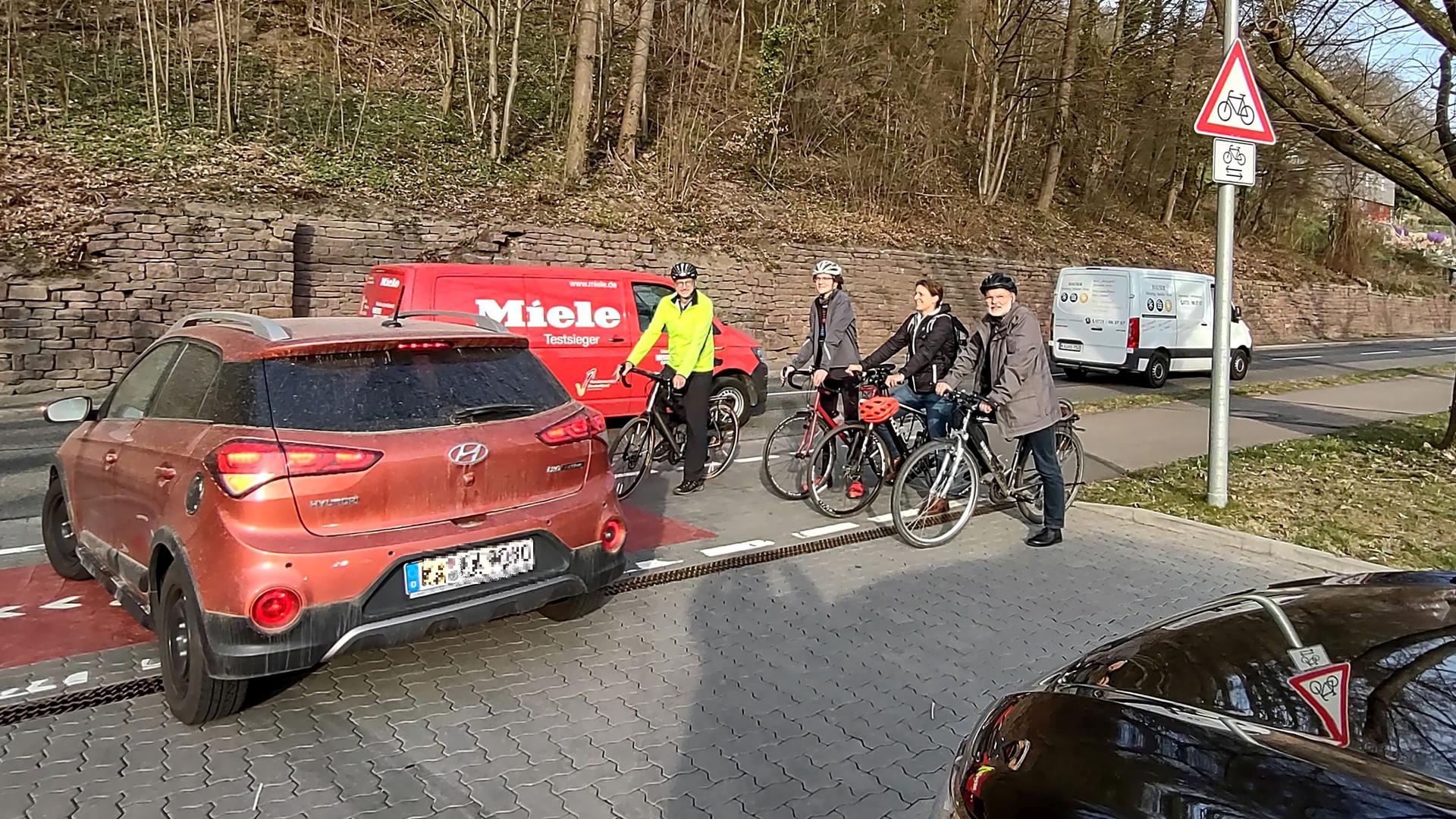 Vier Radfahrer halten auf dem Radweg an der Pforzheimer Straße in Ettlingen, während ein Auto aus einer Ausfahrt auf die Straße fährt.