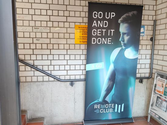 „Geh hoch und mach es fertig“ steht übersetzt auf dem Banner am Treppenhaus-Aufgang Richtung Remote Fitness-Studio. 