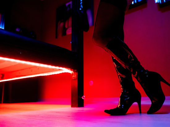 Eine Prostituierte steht vor der roten Beleuchtung unter einem Bett in einem Studio.