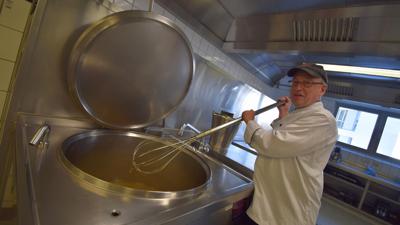 Koch Bernd Schaudel hält in der Großküche der SRH Klinikums Karlsbad einen Kesselrührbesen über einem großen Suppentopf.