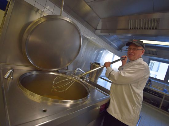 Koch Bernd Schaudel hält in der Großküche der SRH Klinikums Karlsbad einen Kesselrührbesen über einem großen Suppentopf.