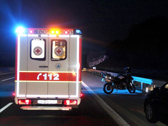Ein Rettungswagen auf der Autobahn, daneben steht ein Motorrad. 