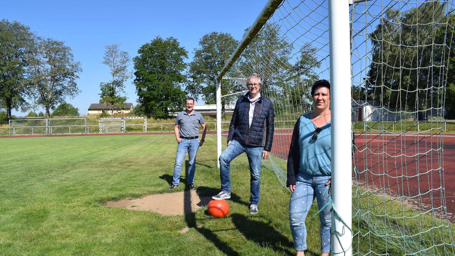 Drei Vereinsvertreter posieren auf einem Fußballfeld im Tor
