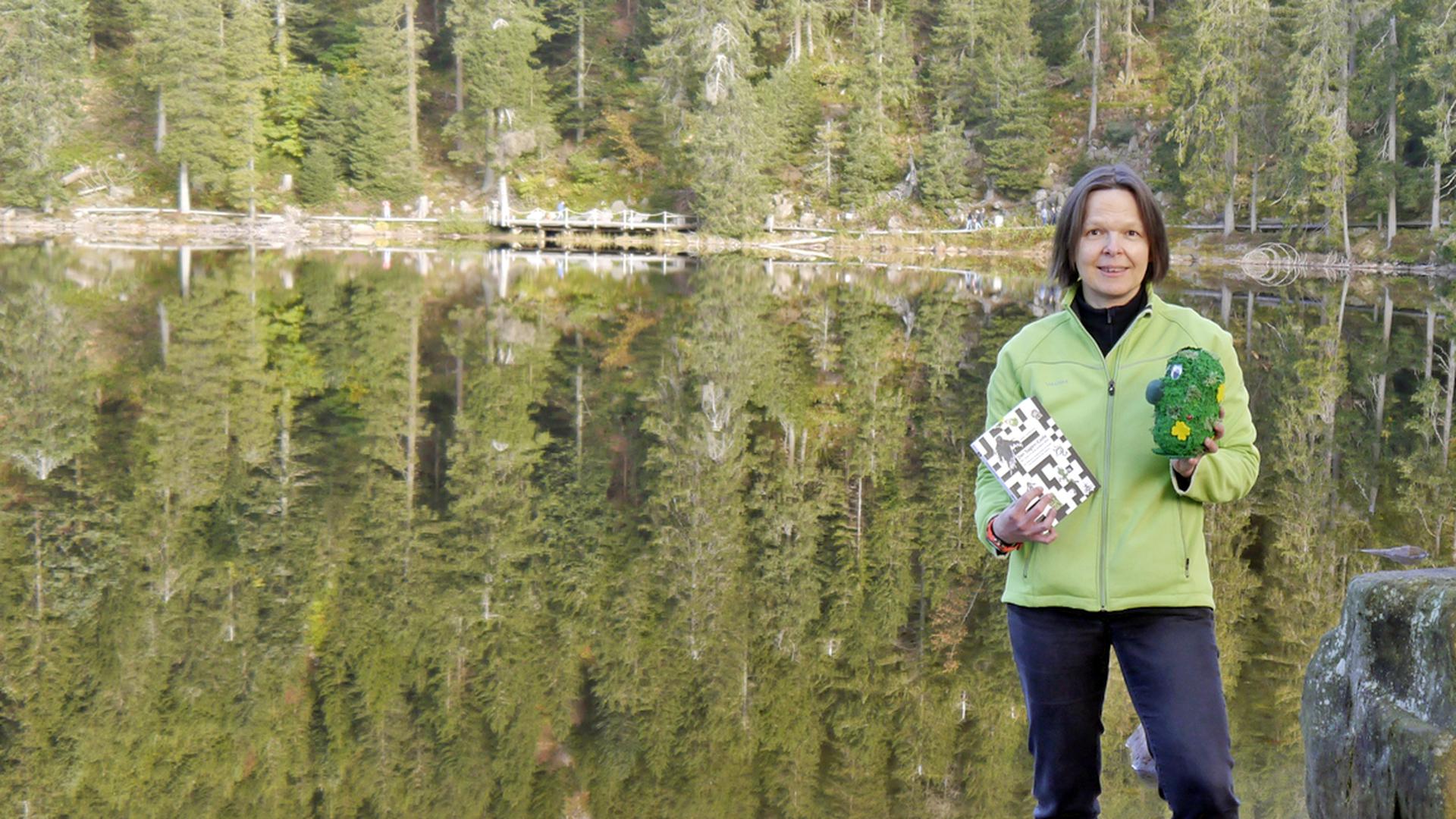 Autorin Beate Hackenberg steht mit ihrem Buch „Der Sagen-Code“ und einem „Mummel“ am Mummelsee.