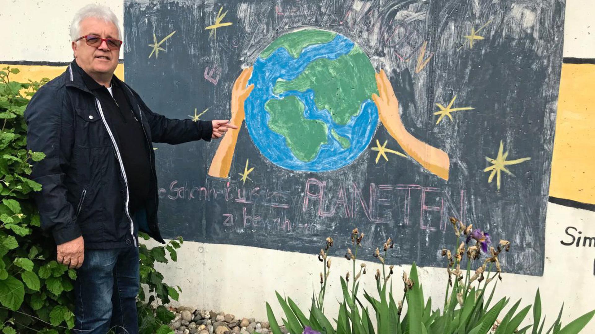 Franz Vogel mit einem Wandbild an seinem Kompostwerk, darauf steht: "Es liegt in unseren Händen, die Schönheit unseres Planeten zu bewahren."