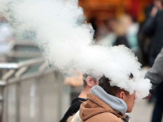 Ein junger Mann atmet den Dampf einer E-Zigarette aus.